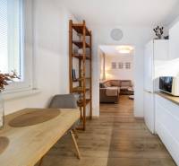 Kuchyně v 2-pokojovém bytě s jídelním stolem, policí a podlahou s dřevěným dekorem.