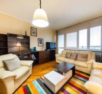 Obývací pokoj v 3-pokojovém bytě s pohovkami, barevným kobercem a podlahou s dřevěným dekorem.