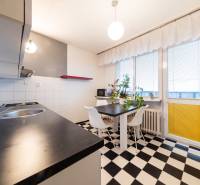 Kuchyně ve 3-pokojovém bytě s černobílou dlažbou, jídelním stolem a velkými okny.