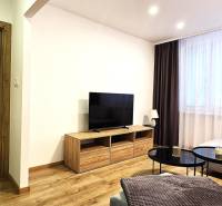 Obývací pokoj v 3-pokojovém bytě s podlahou s dřevěným dekorem a velkou televizí.