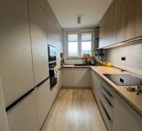 Kuchyně ve 4-pokojovém bytě s podlahou s dřevěným dekorem, světlé skříňky, okno.