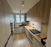 Kuchyně ve 4-pokojovém bytě s linkou, spotřebiči a podlahou s dřevěným dekorem.