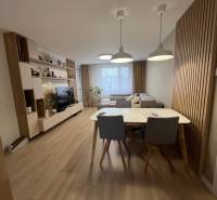 Obývací pokoj ve 4-pokojovém bytě s pohovkou, TV, jídelním stolem a podlahou s dřevěným dekorem.