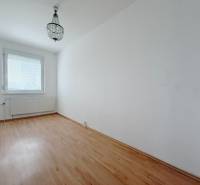 Pokoj ve čtyřpokojovém bytě s lustrem a podlahou s dřevěným dekorem.