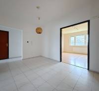 Chodba s dlažbou vede do světlého obývacího pokoje se vstupem na podlahu s dřevěným dekorem.