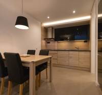 Kuchyně v 2pokojovém bytě s dřevěným dekorem, jídelním stolem a černými židlemi.