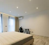 Ložnice v dvoupokojovém bytě s postelí, stolem a podlahou s dřevěným dekorem.