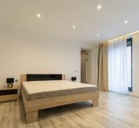 Ložnice v 2pokojovém bytě s postelí, nočním stolkem a podlahou s dřevěným dekorem.