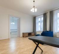 Obývací pokoj v 3-pokojovém bytě s podlahou s dřevěným dekorem a modrou sedačkou.