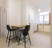 Kuchyně ve 3-pokojovém bytě s barovým pultem, dvěma židlemi a velkým oknem.