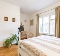 Světlá ložnice s podlahou s dřevěným dekorem, rostlinami a velkými okny ve 2pokojovém bytě.