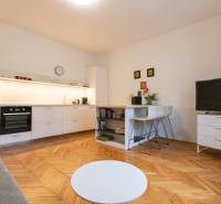 Obývací pokoj v 2pokojovém bytě s kuchyní, podlaha s dřevěným dekorem, TV a stolek.