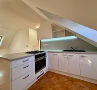 Světlá kuchyně s podkrovním oknem, rohovou pracovní deskou a keramickou dlažbou v 2-pokojovém bytě.