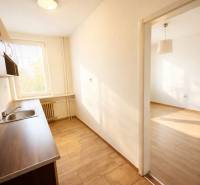 Kuchyně v 1-pokojovém bytě s podlahou s dřevěným dekorem a světlem z okna.