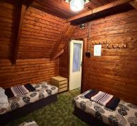 Interiér chaty s dřevěným obložením, postelemi a lustrem, útulné prostředí pro relaxaci.