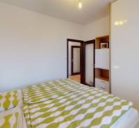 Ložnice ve 4pokojovém bytě s postelí, zeleným povlečením a vestavěnou skříní.