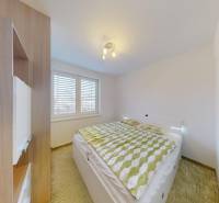 Ložnice ve 4pokojovém bytě s postelí, vestavěnou skříní a podlahou s dřevěným dekorem.