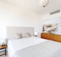 Ložnice v třípokojovém bytě s velkou postelí, obrazem a dřevěnou komodou.