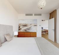 Ložnice s čalouněným čelem, obrazem nad komodou a skleněnými dveřmi ve 3-pokojovém bytě.