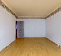 Pokoj v 3-pokojovém bytě s podlahou s dřevěným dekorem a bílými stěnami.