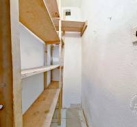 Úzká komora s dřevěnými policemi v 3-pokojovém bytě, bílé stěny.