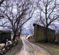 Blátová cesta v Krásnohorskom Podhradí na Mírové ulici, obklopená stromy a budovami. Pozemky - bydlení.