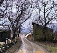 Blátivá cesta s kalužemi vede kolem stodol v Krásnohorskom Podhradí na Mírové. Pozemky - bydlení.