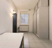 Pokoj v rodinném domě s postelí, šatníkem a oknem, podlaha s dlažbou.