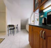 Kuchyně v rodinném domě s dřevěnými skříňkami, stolem a dvěma černými židlemi.