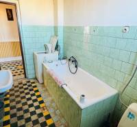 Koupelna v rodinném domě s vanou, umyvadlem a světle zelenými obklady.