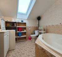 Koupelna v rodinném domě s vanou, pračkou, regálem a střešním oknem.