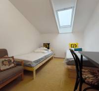 Pokoj v rodinném domě se střešním oknem, dvěma postelemi a křeslem.