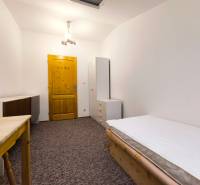 Pokoj v rodinném domě s postelí, skříní a stolem, doplněný bílým osvětlením a kobercovou podlahou.