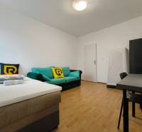 Pokoj v rodinném domě s postelí, pohovkou a pracovním stolem, podlaha s dřevěným dekorem.