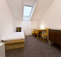 Jednoduchý pokoj s jednolůžkovou postelí, stolem a židlemi v rodinném domě.