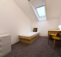 Jednoduchý pokoj s jedním lůžkem, stolem a komodou v rodinném domě.