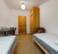 Pokoj v rodinném domě s postelemi, stolem, skříní a židlí.