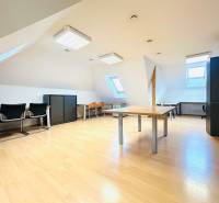 Podkrovní kanceláře s podlahou s dřevěným dekorem, střešními okny a kancelářským zařízením.