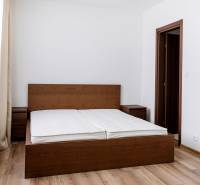 Ložnice v 3-pokojovém bytě s postelí z tmavého dřeva a podlahou s dřevěným dekorem.