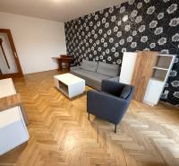 Obývací pokoj ve 3-pokojovém bytě s podlahou s dřevěným dekorem, vzorovanou tapetou a nábytkem.