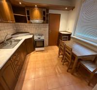 Kuchyně 3pokojového bytu s dřevěným dekorem skříněk a jídelním sezením.