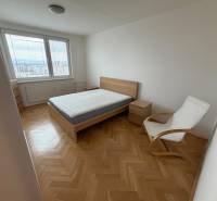 Ložnice s postelí, křeslem a výhledem. Podlaha s dřevěným dekorem v 3-pokojovém bytě.