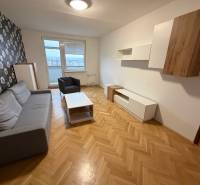 Obývací pokoj v 3-pokojovém bytě s šedou sedací soupravou a květinová tapeta na stěně.