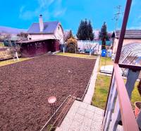 Upravená zahrada u chaty v Partizánském, s vyvýšenými záhony a stromy kolem.