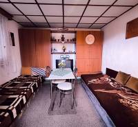 Interiér chaty s postelemi, stolkem, skříňkami a dekoracemi.