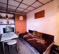 Interiér chaty s pohovkou, jídelním stolem a vestavěnou skříní, dominuje přírodní paleta barev.