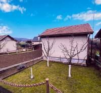 Zahrada s chatou v Partizánském, ovocné stromy a obdělávaná půda, jasná obloha.