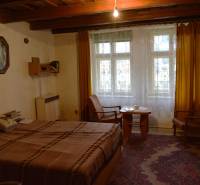 Pokoj v rodinném domě s postelí, křesly, žlutými závěsy a kobercem.