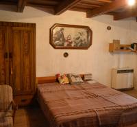 Ložnice v rodinném domě s dřevěnou skříní, postelí a obrazem na stěně.