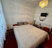 Ložnice v 3-pokojovém bytě s postelí, lustrem a televizorem na stěně.